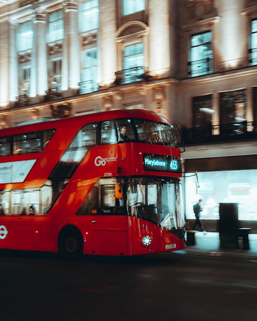 A red double-decker London bus with the destination display reading 'Marylebone' is moving along a street lined with historic, ornate buildings featuring large windows and decorative facades. The bus is part of the Go London service and is captured in motion, with slight blurring indicating movement. Inside the bus, visible through the windows, are passengers seated and standing. The street scene includes pedestrians walking on the pavement near the bus stop, with some waiting or passing by, and others walking past the buildings. The image is lit with natural daylight, highlighting the architecture and vibrant red of the bus, which is associated with London transport. This scene reflects urban mobility typical of central London and subtly connects to house removals and furniture transport services, like those provided by Marylebone Man and Van, especially in the context of home relocation on Marylebone High Street.
